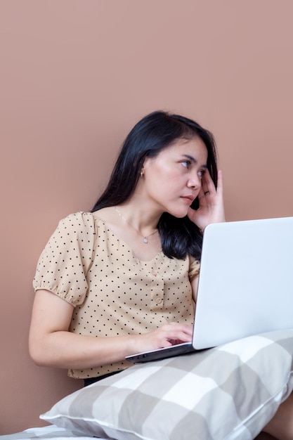 Mujer con laptop en la cama con las manos sosteniendo la cabeza