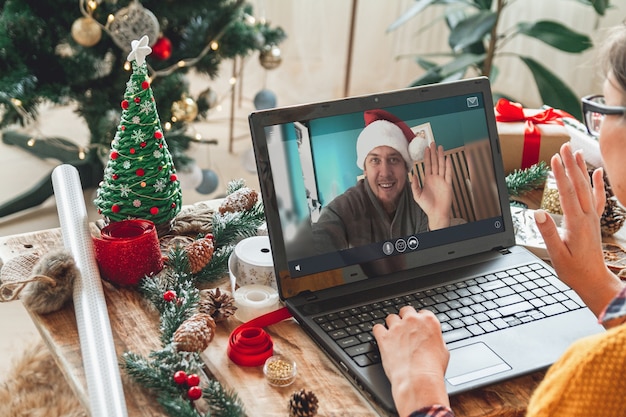 Mujer con laptop cerca del árbol de Navidad acepta felicitaciones en línea