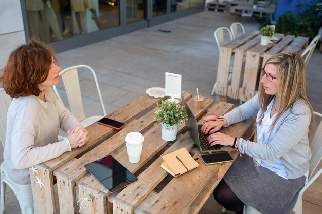 Mujer con laptop reunida con una clienta en una cafetería