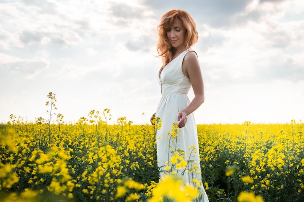 Mujer con un largo vestido amarillo caminando por el campo con flores amarillas al atardecer