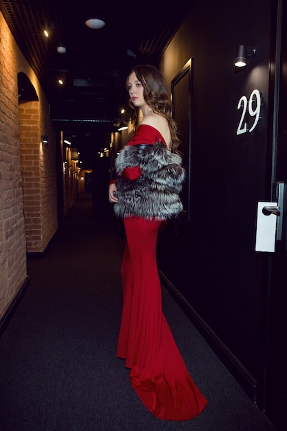 Foto una mujer con un largo vestido rojo y un abrigo de piel se encuentra en un largo y oscuro corredor del hotel