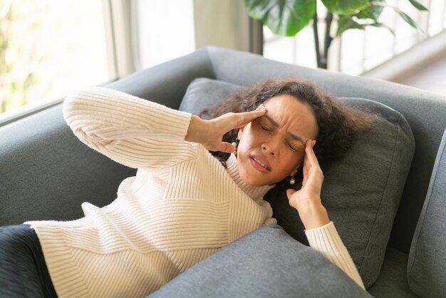 Mujer latina acostada en el sofá en casa con dolor de cabeza