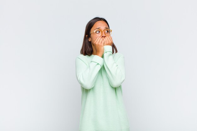 Mujer latina con aspecto preocupado, ansioso, estresado y asustado, mordiéndose las uñas y mirando al espacio de copia lateral