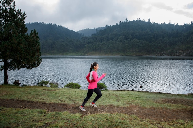 Mujer latina atleta corriendo al aire libre cerca de um lago com montanhas ao fundo