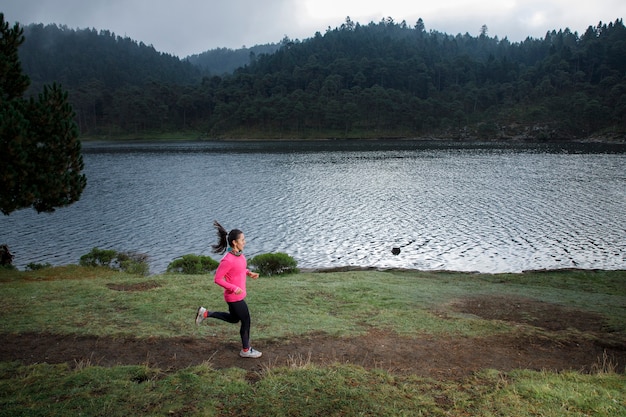 Mujer Latina Atleta corriendo al aire libre cerca de un lago con montanas al fondo