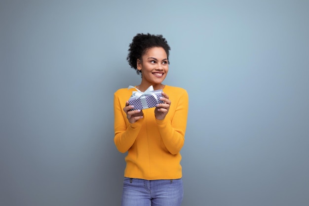 Mujer latina bastante alegre con cabello afro en suéter amarillo casual recibió un regalo de cumpleaños