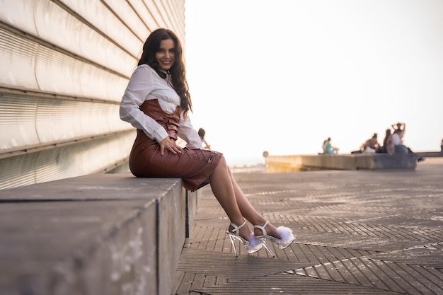 Mujer latina bastante morena en una falda de cuero sentada en la ciudad en una puesta de sol