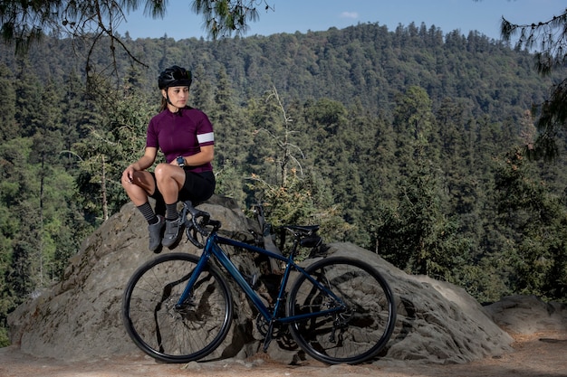 Mujer latina con bicicleta descansando en el bosque con un paisaje de árboles en el fondo