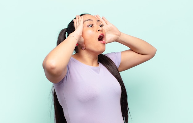 Mujer latina con la boca abierta, con aspecto horrorizado y conmocionado por un terrible error, levantando las manos a la cabeza.