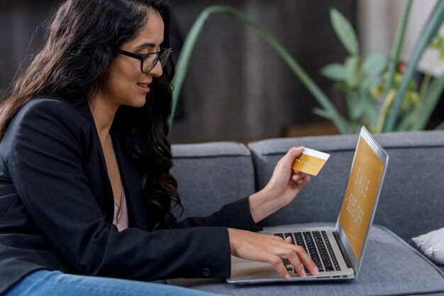 Mujer latina comprando en line desde su casa en su laptop y pagando con su tarjeta de credito