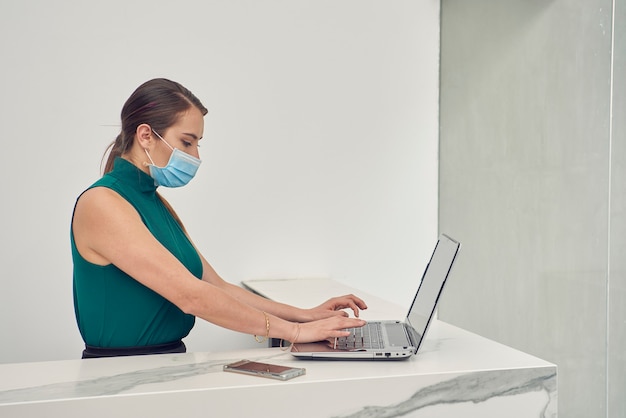 mujer latina con cubrebocas trabajando en su laptop en la recepcion