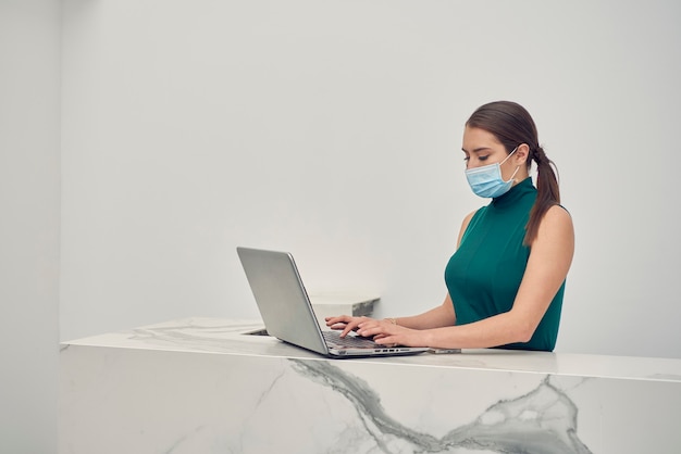 mujer latina con cubrebocas trabajando en su laptop en la recepcion