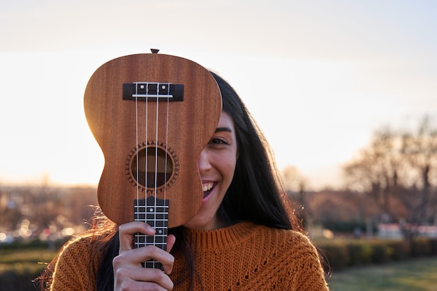 mujer latina, cubierta, ella, cara, con, ukelele, sonriente, mujer joven, con, morena, pelo