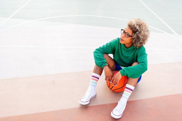 Mujer latina descansando mientras se sienta en la cancha después de la práctica de baloncesto concepto de deporte urbano al aire libre copia espacio para texto