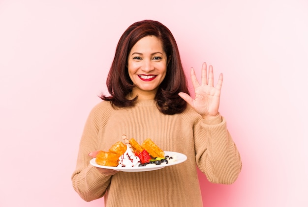 La mujer latina de la Edad Media que sostenía una galleta aisló la sonrisa alegre que mostraba el número cinco con los dedos.