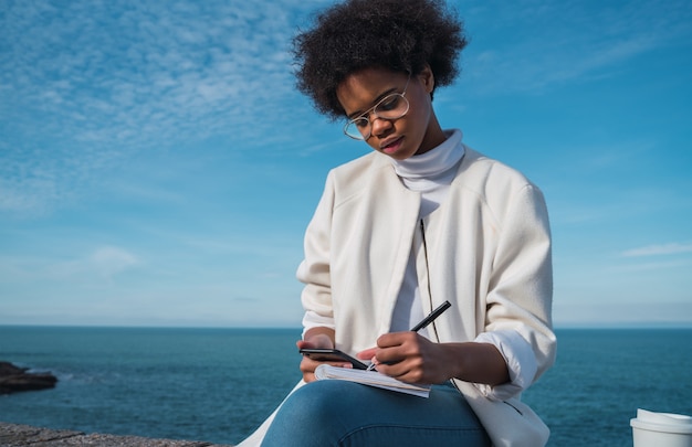 Mujer latina escribiendo algo al aire libre.