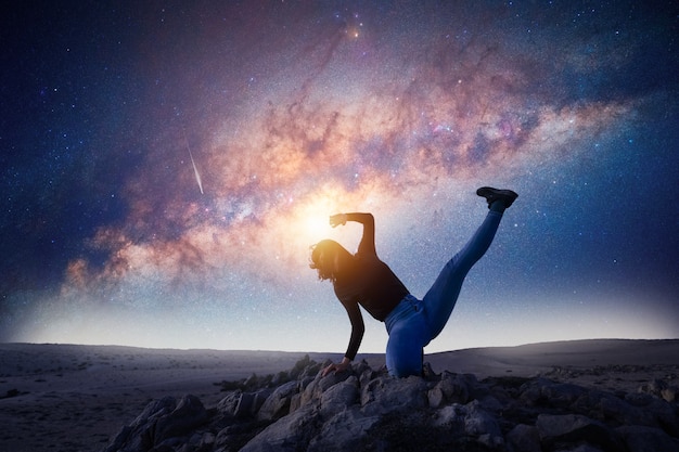 La mujer latina está bailando o posando en la cima de la montaña por la noche con el fondo de la Vía Láctea