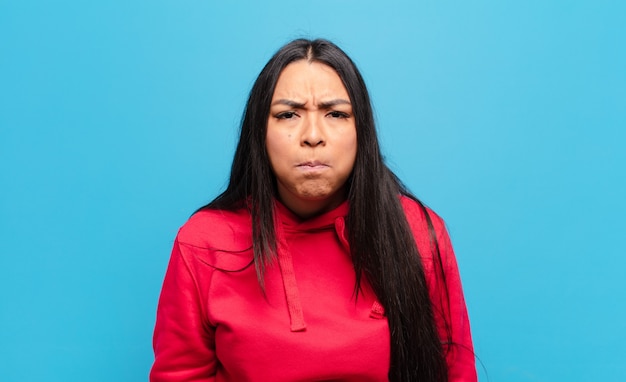 Mujer latina con una expresión tonta, loca y sorprendida, mejillas hinchadas, sintiéndose rellena, gorda y llena de comida