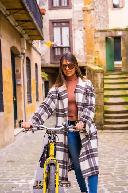 Mujer latina con gafas de sol haciendo turismo en bicicleta en la ciudad a través del casco antiguo Estilo de vida ecoturístico en primavera