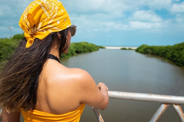 Mujer latina con gafas de sol y pañuelo en la cabeza contemplando la desembocadura del río conociendo el océano