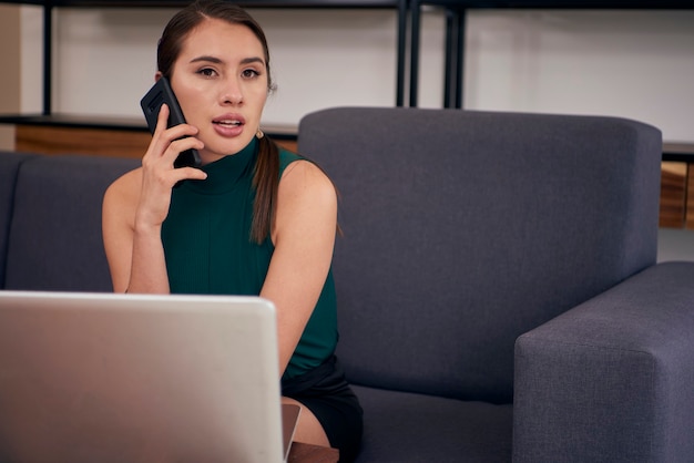 Mujer latina hablando por telefono mientras trabaja en su casa con su computadora