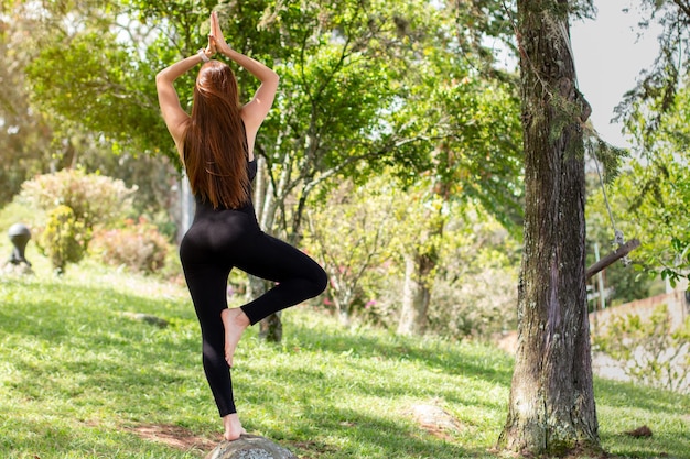 Mujer latina haciendo yoga en un parque natural y vistiendo ropa cómoda.