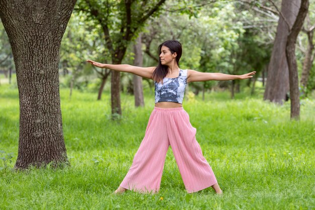 Mujer latina haciendo yogaasanas con diferentes posturas en el parque al aire libre con césped y árboles en el ...