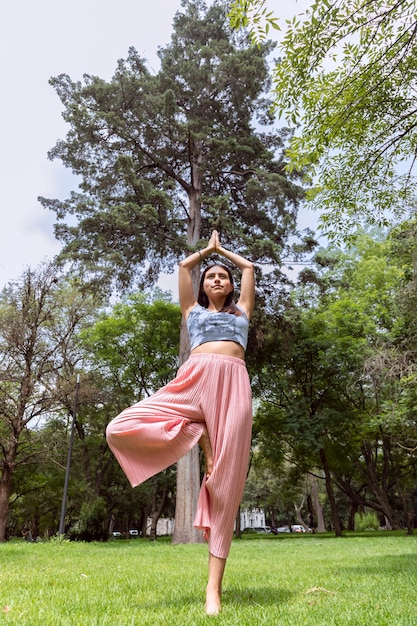 Mujer latina haciendo yogaasanas con diferentes posturas en el parque al aire libre con césped y árboles en el ...