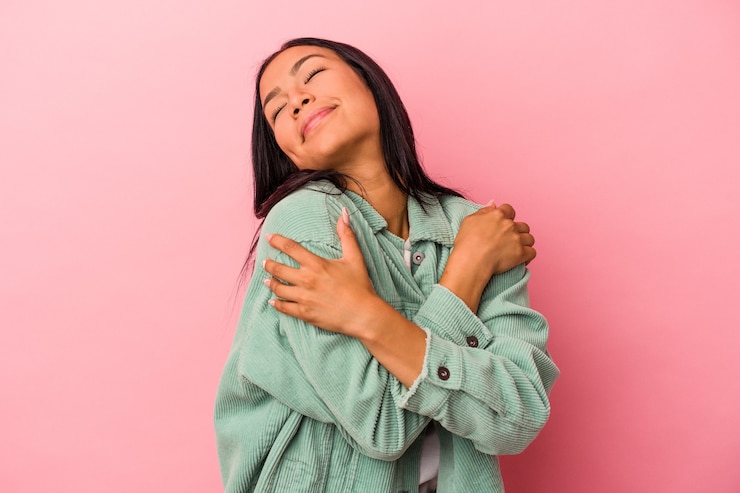 Foto mujer latina joven aislada en abrazos de fondo rosa, sonriendo despreocupada y feliz.
