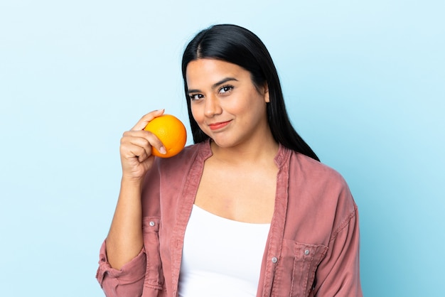 Mujer latina joven aislada en azul con una naranja