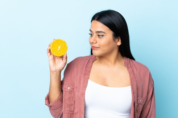 Mujer latina joven aislada en azul con una naranja