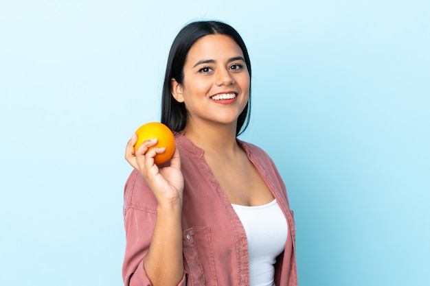 Mujer latina joven aislada en azul con una naranja