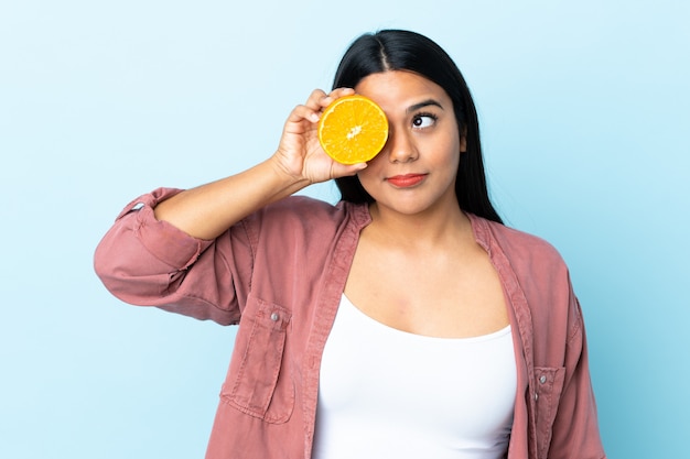 Mujer latina joven aislada en azul con una naranja