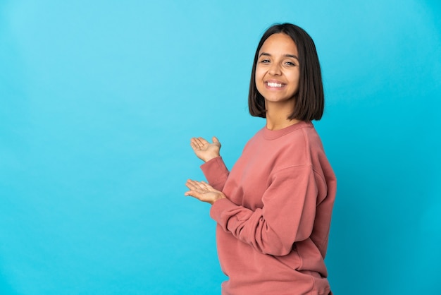 Mujer latina joven aislada en la pared azul extendiendo las manos hacia el lado para invitar a venir