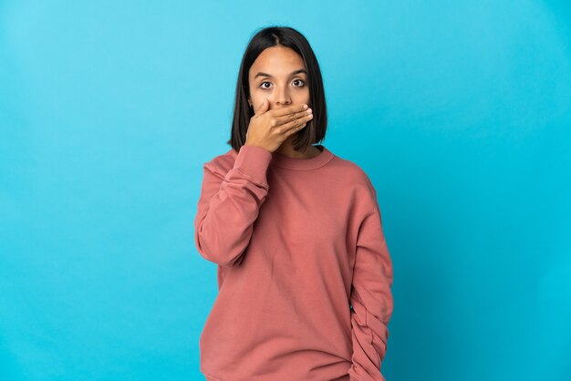 Mujer latina joven aislada en la pared azul que cubre la boca con la mano