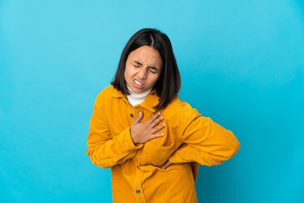 Mujer latina joven aislada en la pared azul que tiene un dolor en el corazón