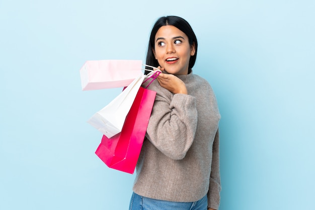 Mujer latina joven aislada en la pared azul sosteniendo bolsas de compras y sonriendo