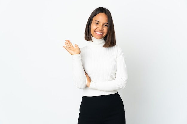 Foto mujer latina joven aislada en la pared blanca saludando con la mano con expresión feliz