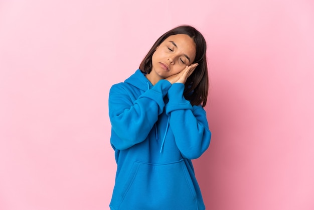 Mujer latina joven aislada en la pared rosada haciendo gesto de sueño en expresión adorable