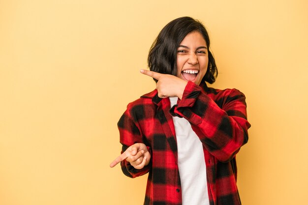 Mujer latina joven aislada sobre fondo amarillo apuntando con los dedos índices a un espacio de copia, expresando entusiasmo y deseo.