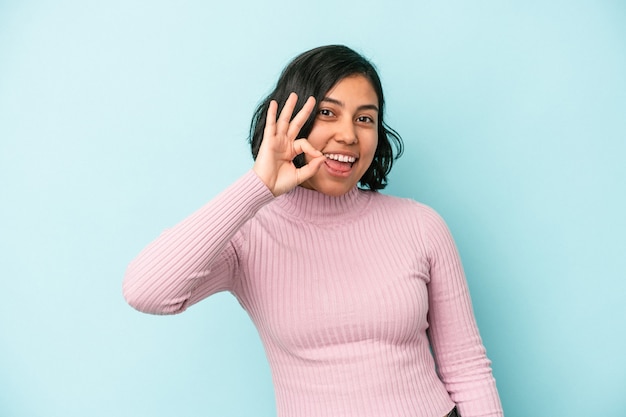 Mujer latina joven aislada sobre fondo azul alegre y confiado mostrando gesto ok.