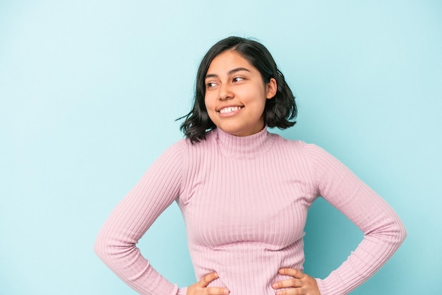 Foto mujer latina joven aislada sobre fondo azul confiado manteniendo las manos en las caderas.