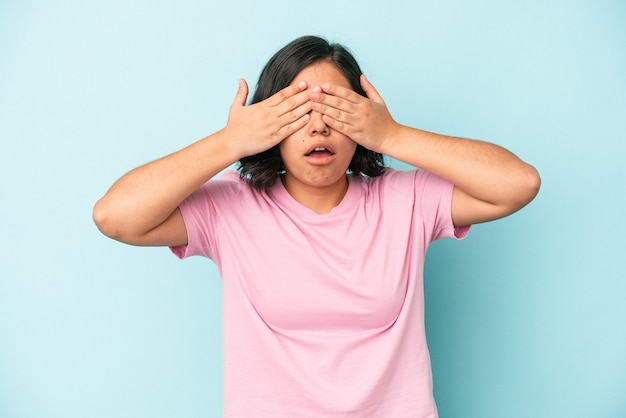 Mujer latina joven aislada sobre fondo azul miedo cubrirse los ojos con las manos.