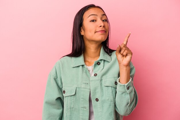 Mujer latina joven aislada sobre fondo rosa que muestra el número uno con el dedo.