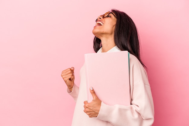 Mujer latina joven estudiante aislada sobre fondo rosa levantando el puño después de una victoria, concepto ganador.