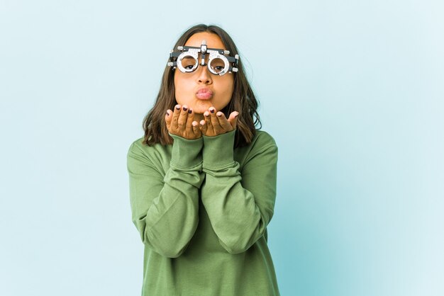 Mujer latina joven oculista sobre pared aislada doblando los labios y sosteniendo las palmas para enviar beso al aire.