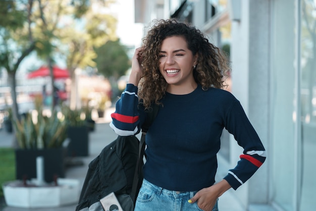 Mujer latina joven con el pelo rizado sonriendo mientras camina al aire libre en la calle. Concepto urbano.