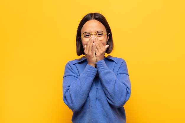 Foto mujer latina joven que parece feliz, alegre, afortunado y sorprendido cubriendo la boca con ambas manos