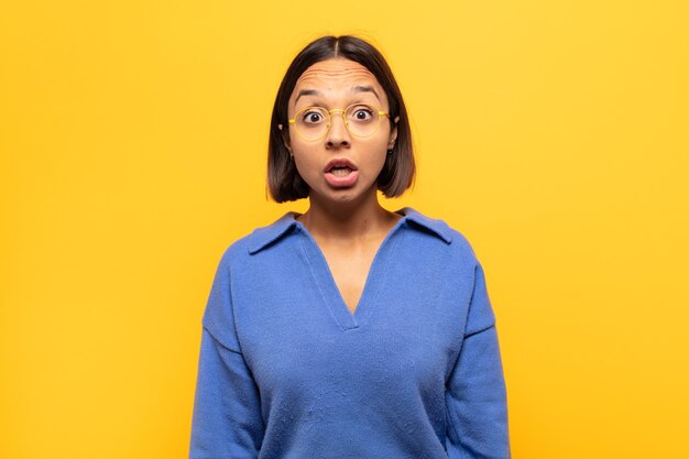 Mujer latina joven que parece muy conmocionada o sorprendida, mirando con la boca abierta diciendo wow