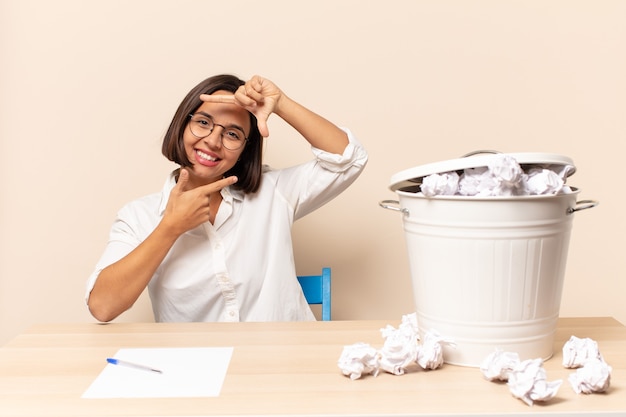 Mujer latina joven que se siente feliz, amable y positiva, sonriendo y haciendo un retrato o marco de fotos con las manos